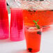 A close up of a Fineline Savvi Serve neon red plastic tumbler filled with red punch, fruit, and mint leaves.