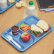 A blue Carlisle 6 compartment tray with a sandwich and fruit on it.