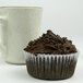 A white fluted baking cup with a chocolate cupcake with chocolate frosting and chocolate sprinkles.
