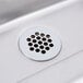 A stainless steel die stamped drip pan with a circular drain in a sink.