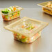 A Vollrath 1/6 size amber high heat plastic food pan filled with vegetables on a table in a room with more plastic containers of food.