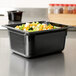 A Vollrath black plastic food pan with vegetables in it on a counter.