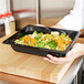 A person holding a Vollrath black plastic food pan filled with broccoli and carrots.