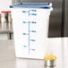 A white Cambro CamSquares food storage container with blue lid filled with pasta and a measuring cup.
