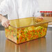 A chef holding a Vollrath amber plastic food pan filled with vegetables.