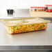 A Vollrath amber plastic food pan on a counter filled with vegetables.