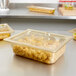 A clear plastic Vollrath food pan filled with food on a counter.