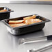 A black Vollrath plastic food pan with food on a counter.
