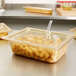 A Vollrath plastic container with food on a salad bar counter with a slotted amber plastic lid.