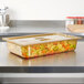 A Vollrath amber plastic cover on a full food pan of vegetables on a counter.
