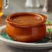 An Acopa brown stoneware onion soup bowl filled with soup on a plate on a restaurant table.