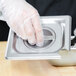 A person wearing plastic gloves holding a Vollrath stainless steel slotted cover over a metal tray.
