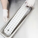 A person in white gloves holding a Vollrath stainless steel drain tray over a white background.
