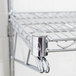 An Advance Tabco chrome wire shelf with metal hooks on the end.