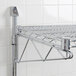 An Advance Tabco chrome wire shelf mounted on a white tile wall.