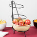 A Cal-Mil iron black three tier round bowl stand with bowls of fruit on a table.