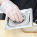 A hand in a plastic glove holding a stainless steel Vollrath 1/6 size pan cover.