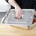 A person holding a Vollrath stainless steel pan cover over food on a metal tray.