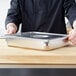 A person holding a Vollrath stainless steel steam table pan cover.