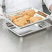 A person holding a tray of fried chicken in a Vollrath stainless steel hotel pan.
