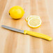 A Victorinox utility knife with a yellow handle slicing a lemon on a table.