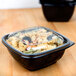 A black plastic Sabert deli bowl filled with pasta on a counter.