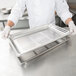 A chef holding a Vollrath stainless steel table pan on a tray.