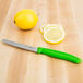 A Victorinox utility knife with a green handle cutting a lemon on a table.