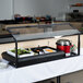 A Carlisle black adjustable single sneeze guard over food on a table with food in containers.