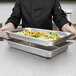 A chef holding a Vollrath stainless steel steam table pan filled with vegetables.