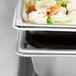 A Vollrath stainless steel steam table pan with food including a blurry carrot slice.