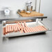 A Vollrath stainless steel tray with hot dogs on a counter.