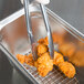 A pair of metal tongs holding fried chicken over a Vollrath stainless steel wire pan grate.