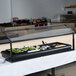A Carlisle black adjustable single sneeze guard over a buffet table with food in it.