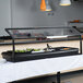 A Carlisle black adjustable single sneeze guard on a buffet table with food.