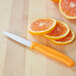 A Victorinox paring knife with an orange handle next to sliced oranges.