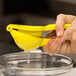 A person using a yellow Saf-T-Grip lemon squeezer to juice a lemon.