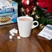 A mug of Swiss Miss hot chocolate with marshmallows on a table next to a box of Swiss Miss Hot Chocolate Mix packets.