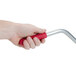 A hand holding a red and silver FMP Coarse Broiler / Grill Cleaning Brush.