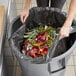 A woman putting a Lavex black trash bag full of fruit into a trash can.
