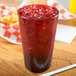 A Carlisle ruby plastic tumbler filled with red liquid and ice with a straw on a wood table.