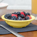 A white SuperMel bowl filled with blueberries and raspberries on a table with a yellow stripe.