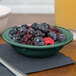 A bowl of blueberries on a table with a bowl of cherries.