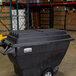 A black Rubbermaid hinged dome lid on a tilt truck in a warehouse.