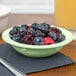 A green GET melamine bowl filled with blueberries and raspberries on a table with a napkin.