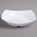 A white square Carlisle melamine bowl on a gray surface.
