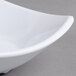 A close-up of a white Carlisle square melamine bowl with a curved edge.