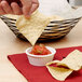 A person holding a tortilla chip and dipping it into a bowl of salsa.