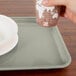 A hand holding a cup over a Cambro rectangular tray with a cup and a plate on it.