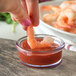 A person holding a shrimp in a Carlisle plastic ramekin of sauce.